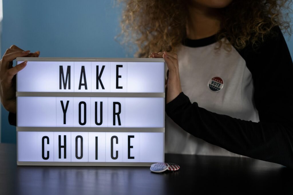 Woman holding lightbox with 'Make Your Choice' promoting civic duty and voting.